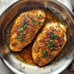 crispy pan fried chicken breasts in stainless steel skillet with herbs