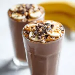 Chocolate banana protein shake in tall glass with toppings