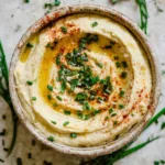 Creamy hummus in a bowl topped with olive oil, chives, and paprika