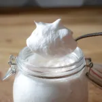 Protein marshmallow fluff on spoon above glass jar, fluffy and creamy