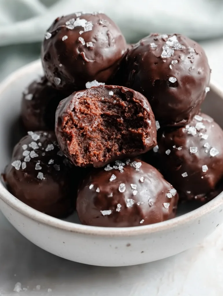High-Protein Brownie Balls — No-Bake, Low Sugar 6 chocolate high-protein brownie balls with sea salt flakes and one bitten open