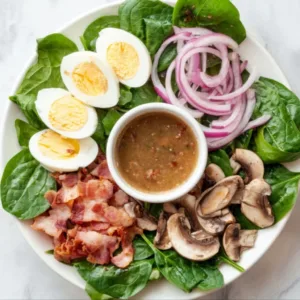 Spinach salad ingredients with warm bacon dressing in bowl