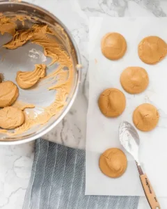 Peanut butter dough shaped into cookies on parchment paper next to mixing bowl