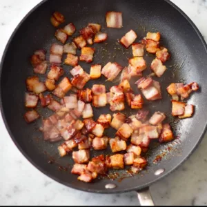 Bacon pieces cooking in skillet for warm bacon dressing