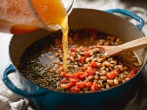 Pouring broth into pot with black eyed peas, tomatoes, and herbs